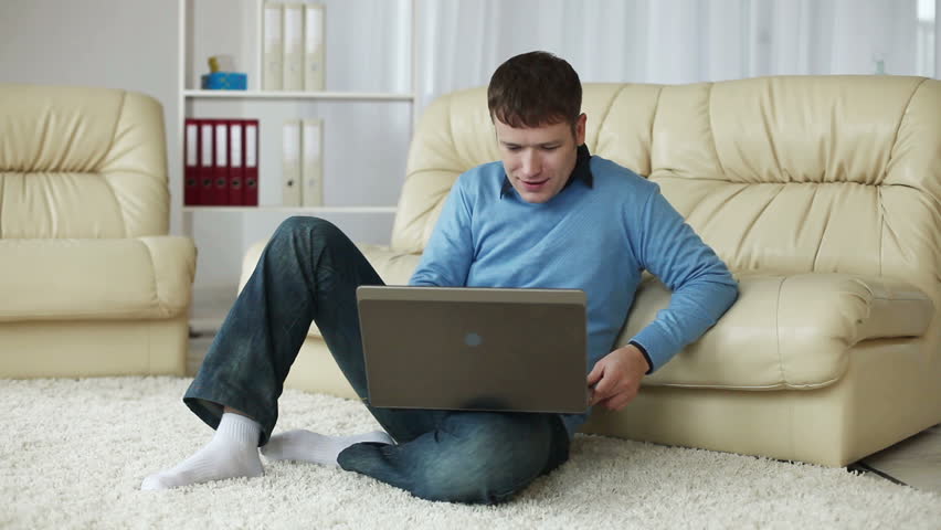 Smilling young man with laptop on carpet. He gets up and walks away 