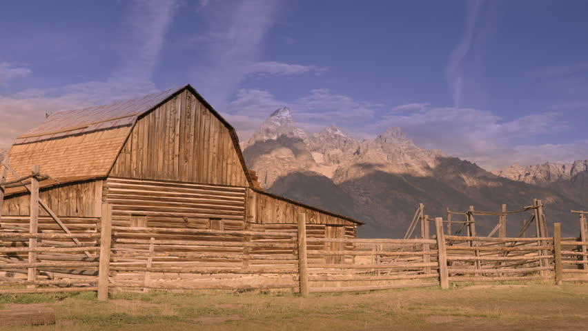Historic pioneer barn in Grand Teton National Park, Wyoming, with autumn colors, blue skies, snowy mountain peaks, and dramatic clouds. 4K.