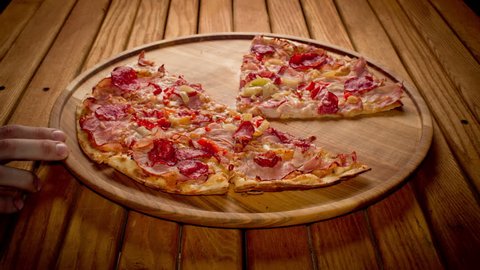 Top view hands taking big pizza cuts from wooden plate on the table - stop motion animation, 4K 