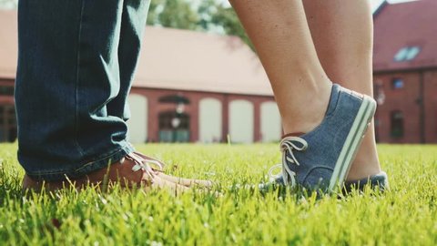 Close up of feet and legs as woman is tip toeing for a kiss. Romantic Couple kissing on a green grass lawn outdoors. Slow Motion 120 fps. Young love concept with lovers kissing. Stylish hipster shoes.