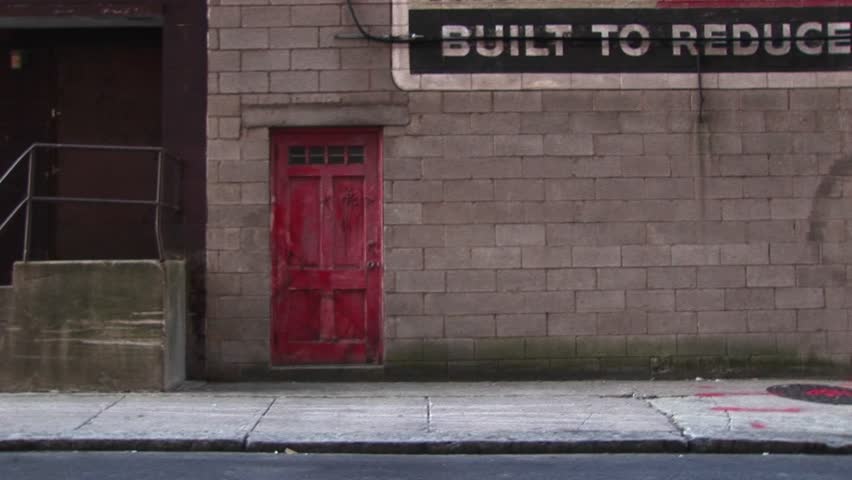 A young man walks by old building with a red door.