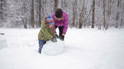 Mother and young son make a snowman in winter park