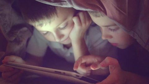 Two kids using tablet pc under blanket at night. Brothers with tablet computer in a dark room. Slow motion HD 1080p