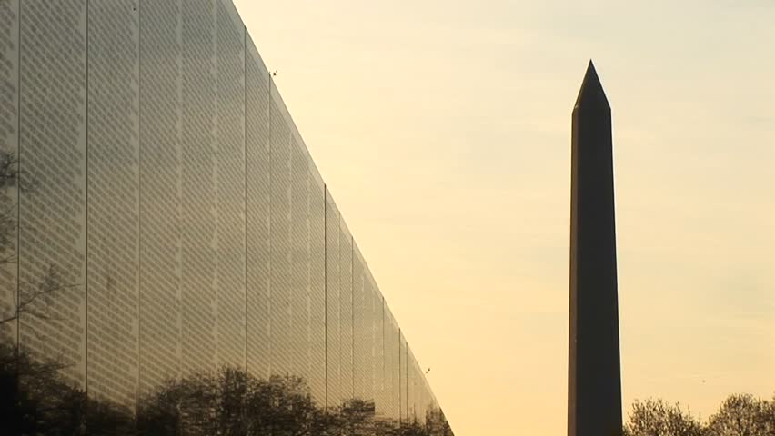 With a golden sky backdrop, the Washington Monument is seen in silhouette next to the Vietnam Memorial Wall.