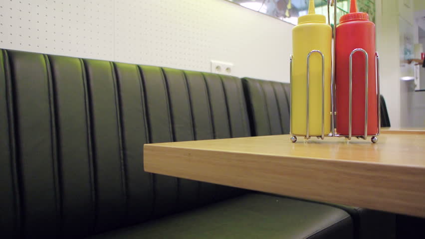 Woman picking mustard bottle instead of ketchup from the next table in the fast-food cafe Americana
