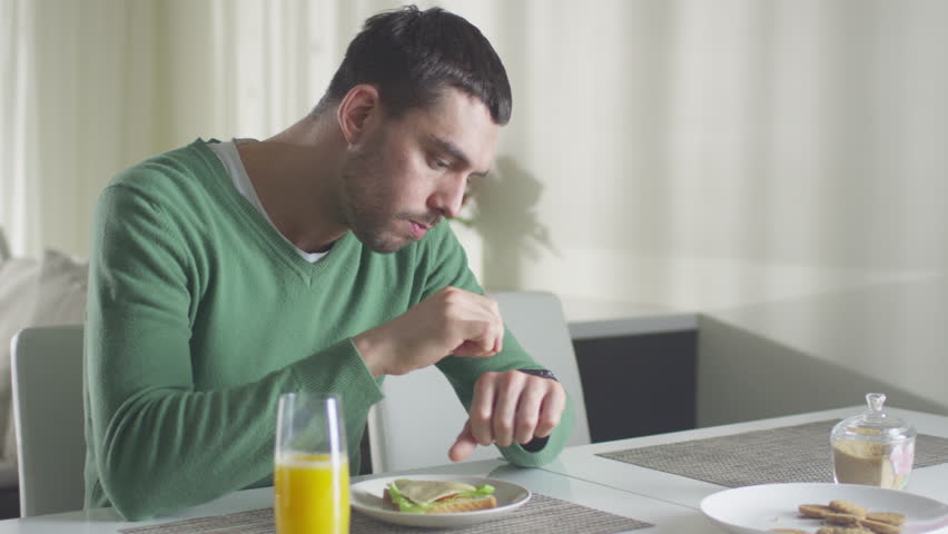Man is checking his smartwatch while having a lunch and orange juice in the morning Shot on RED Cinema Camera in 4K (UHD).