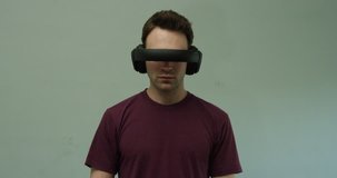 Young man wearing futuristic virtual reality headset scrolls through imaginary interface and screens against clean background, immersed in digital world