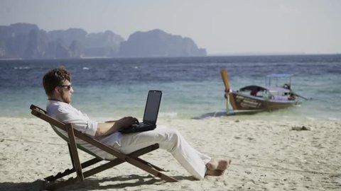 Dream work. Man works on the wonderful beach and enjoys his life. The happiest work. Freelance.