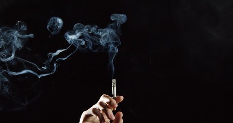 Elegant smoke rises from cigarette in hand, slow motion dramatic spirals, against black background