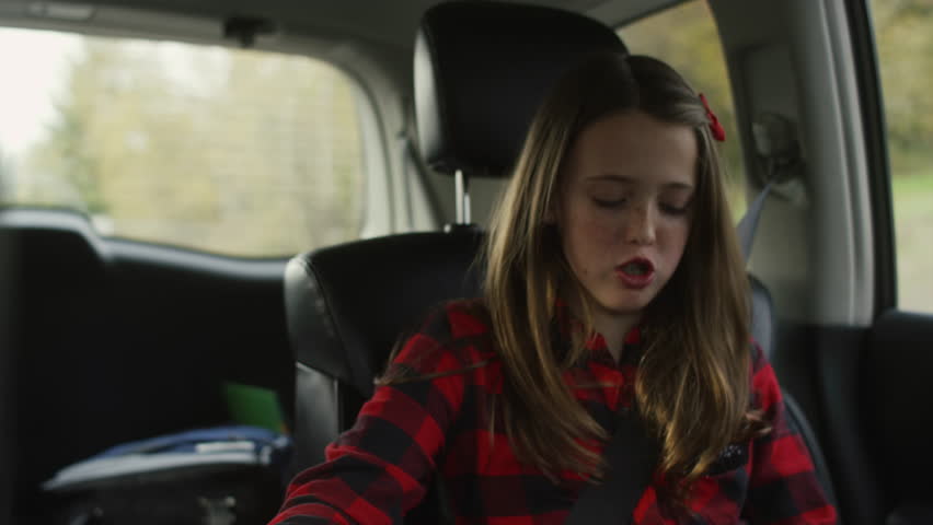 A girl in the back seat of a car talking and eating snacks