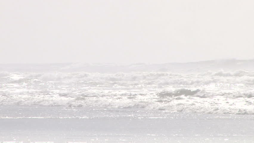 A couple walk in shallow water on the Oregon Coast during hot and humid day.