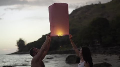 Happy couple in love launches  Chinese lantern  on the beach.  Strong family.