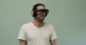 Young man or scientist wearing futuristic virtual reality headset operates invisible computer interface in three dimensions, clicking, scrolling and swiping against green background
