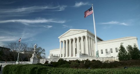 The US Supreme Court wide with flags and blue sky with light clouds. Also available in 4K SLog.