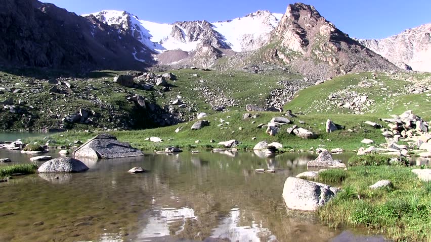 Snow-capped mountains. Boulders and stones at the foot of the mountains. The clear mountain pond. Reflection of snow-covered mountain in the clear lake .. Calm. Blue sky in the mountains.