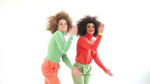 Two funny girls wearing a 70s retro clothes dancing in studio. Disco diva over white background