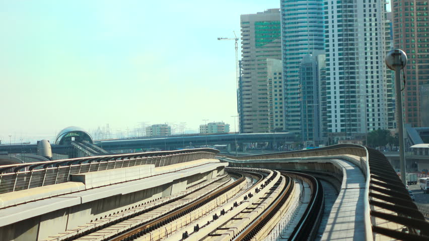 Metro come to station in Dubai. Modern train arrives at metro station. Sun is shining brightly and high towers on the background create futuristic city scape outlook.