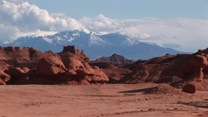 Wide shot of sandstone formations and snow-covered mountains at Goblin Valley State Park in Utah.