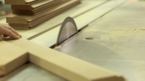 A running blade on a bench saw sawing trough the wooden log in the middle of a working space, close up footage.