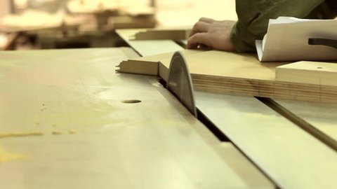 A running blade on a bench saw sawing trough the wooden log in the middle of a working space, close up footage.