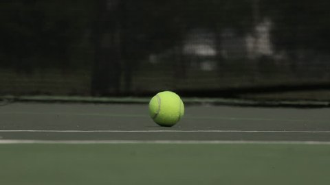 Low level angle shows hand reaching down to pick up a tennis ball on the court.