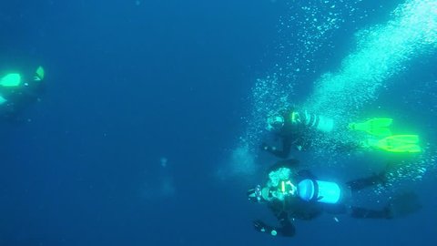 Group of Scuba Divers on a Deep Dive. Scuba Divers Underwater On Blue Background In The Ocean. Slow motion view of scuba divers exhaled oxygen bubbles ascending to the surface.