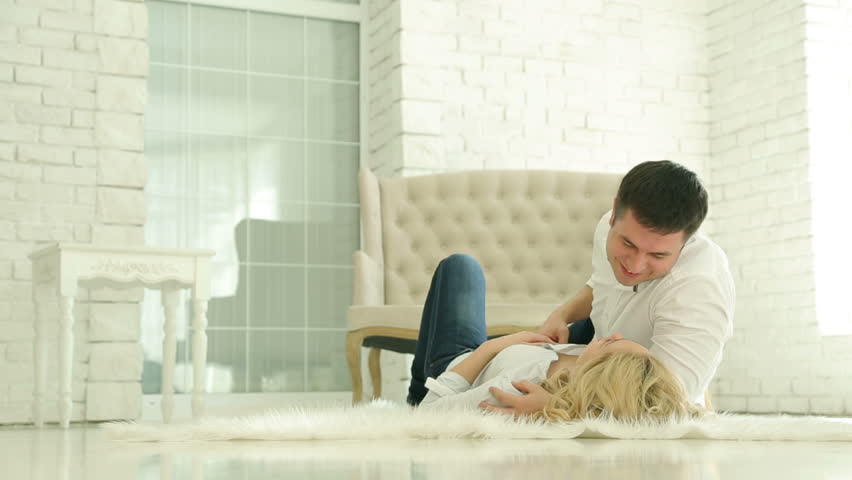 A man and a woman lying on the floor. A woman touches the hand of the man