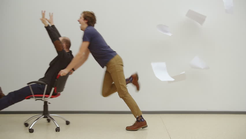 Office chair race. Slow motion. Young guys have fun in the office during a break. Games of businessmen from large offices. Men celebrate a successful deal and throwing papers up. Office party.