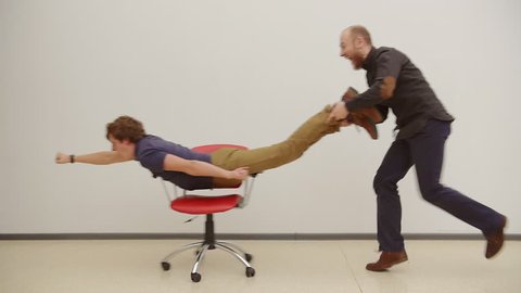 Office chair race. Young guys have fun in the office during a break. Games of businessmen from large offices. Men celebrate a successful deal like superhero. Office business party. Slow motion.