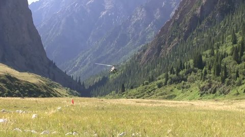 helicopter sits on the ground in a picturesque mountain gorge.  clear sunny day, mountains in the distance covered in a haze