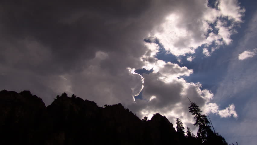 Time lapse of clouds including mountain range and trees.