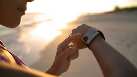 Woman touching smartwatch on beach during sunset. Closeup of female using smart watch app outdoors.