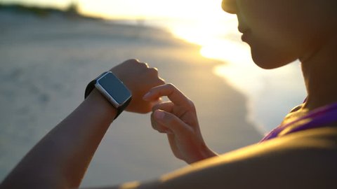 Smartwatch. Young woman using smart watch on beach. Closeup of female touching touch screen on watch entering watch app.