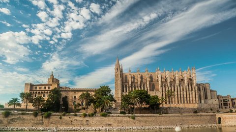 Timelapse with flying clouds over Cathedral of Palma de Mallorca and Almudaina Castle. Beautiful gothic architecture overlooking the sea shore, Mallorca island, Spain.