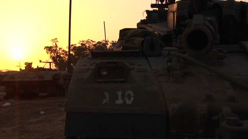 An Israeli tank is silhouetted against a colorful sky.