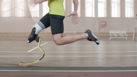 Tracking shot of Paralympic athlete with prosthetic leg running on track in slow motion