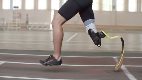 Tracking shot tilt-up of determined Paralympic athlete with prosthetic leg running on track in slow motion