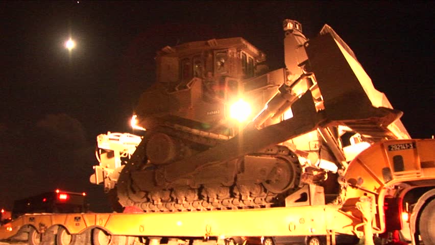 An Israeli armored bulldozer is unloaded from a flatbed truck for night patrol along the Gaza Strip