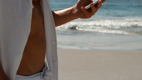 Handsome man wearing white using smartphone on the beach