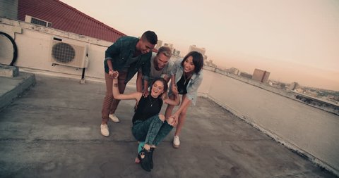 Girl is being pushed on skateboard on the rooftop by a group of friends
