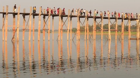 MANDALAY, MYANMAR - JANUARY 17, 2016: Burmese people and monks walking on U Bein Bridge. The bridge is the world longest teak bridge - 1.2 km and built across the Taungthaman Lake.