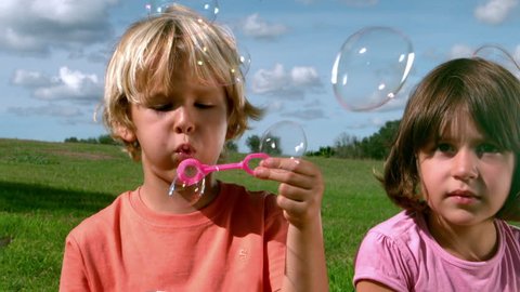 Small boy blowing bubbles with a girl in cinemagraph style Video stock