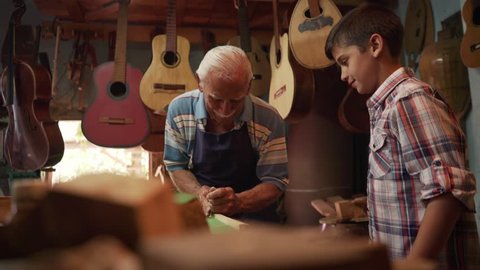 Old and young people showing love for music. Boy and senior man, happy kid and elderly person, grandpa teaching grandchild how to chisel wood for guitars and instruments. Traditional profession
