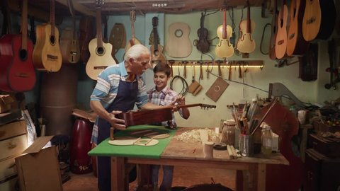 Old and young people showing love for music. Boy and senior man, happy kid and elderly person, grandfather showing guitars and instruments to grandson in lute maker shop. Proud retired worker
