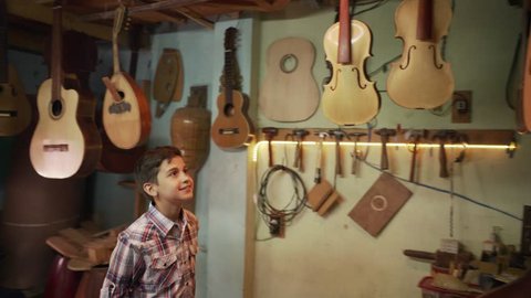 Young people showing love for music. Hispanic boy, happy kid, grandson with guitars and instruments in lute maker shop. Child smiling, looking at classic guitar and musical instrument

