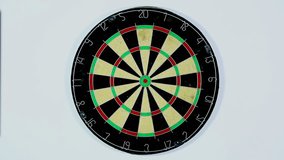 A dart strikes the bulls-eye of a dartboard. Wide shot of a dart board from below, three darts with a bull's eye. 