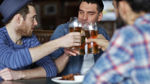 people, toast, leisure, friendship and celebration concept - happy male friends drinking beer and clinking glasses at bar or pub
