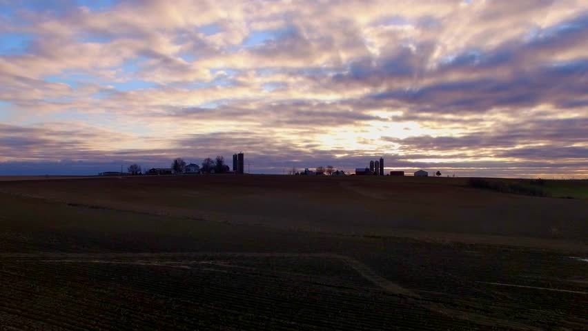 Beautiful Wisconsin dairy farms on horizon at daybreak, silhouetted against colorful sunrise sky.