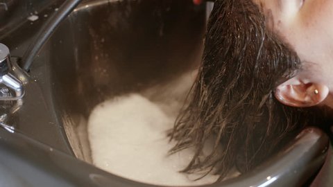 Stylist Rinses a Brunette's Hair at Salon Shampoo Bowl