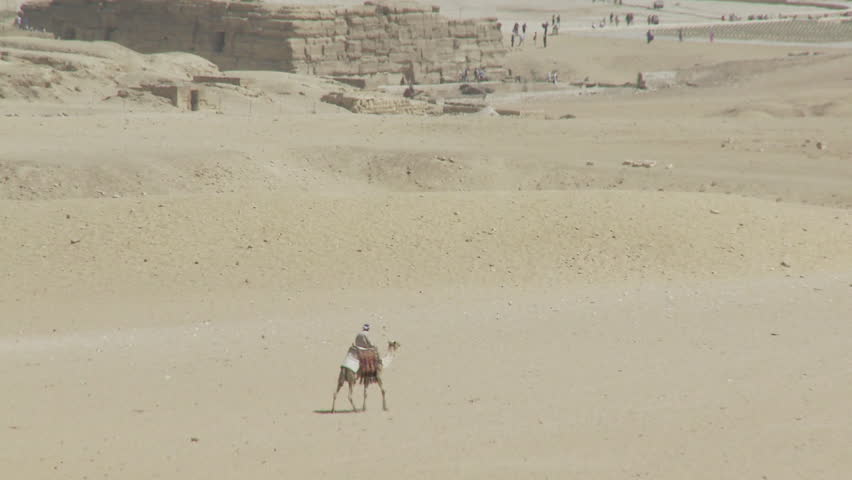 High angled long shot of man on camel walking through desert, past base of pyramids, Giza
 Royalty-Free Stock Footage #15881716